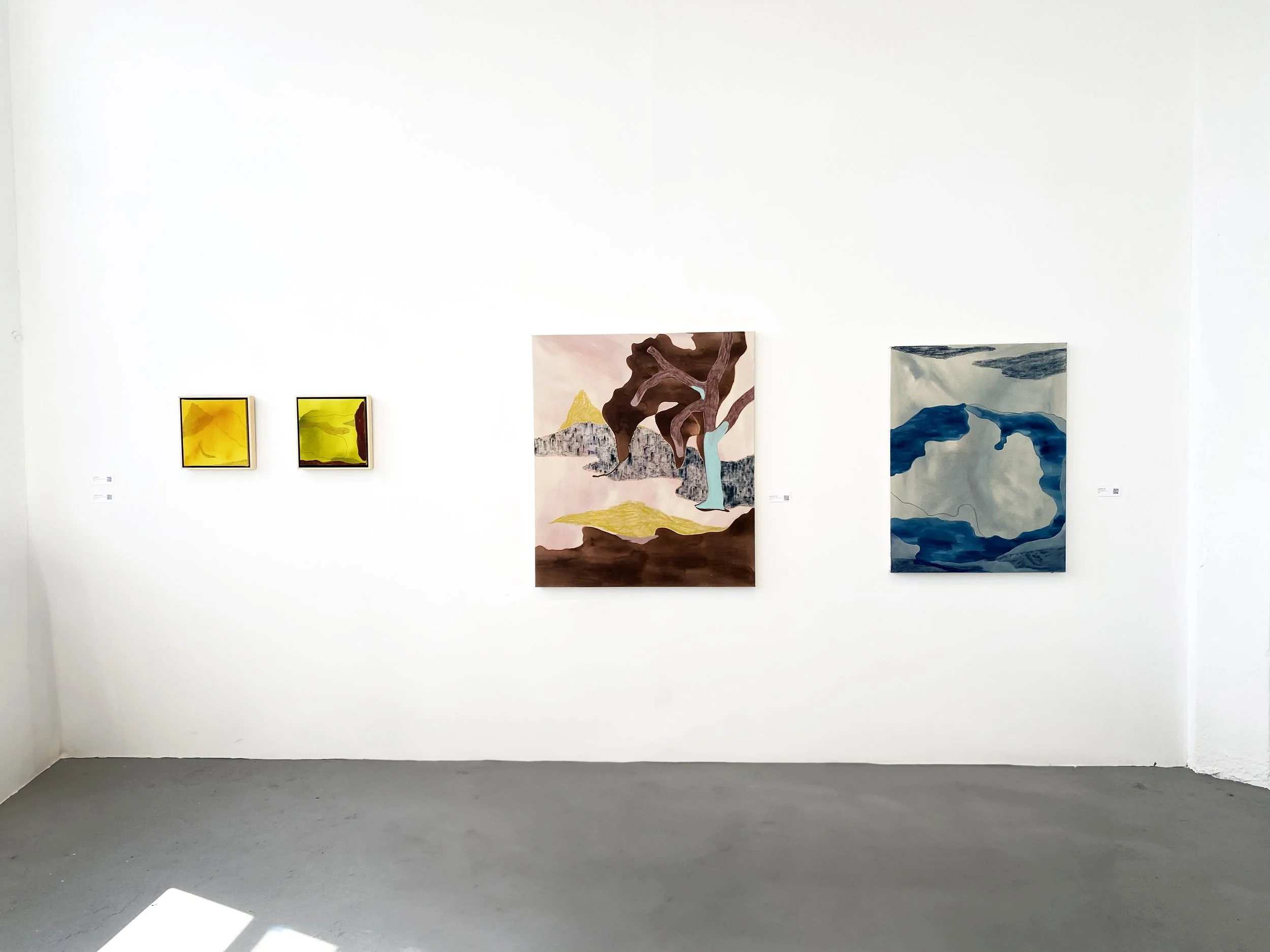 Art gallery wall displaying three abstract paintings; two small square yellow artworks on the left and two larger rectangular pieces in earthy brown and cool blue tones on the right.