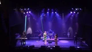 Live band performing on stage with purple lighting and various instruments
