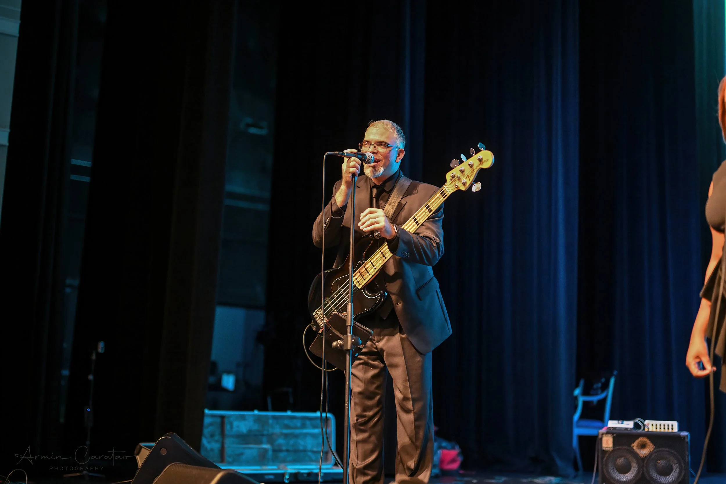 Musician in suit playing bass guitar and singing on stage