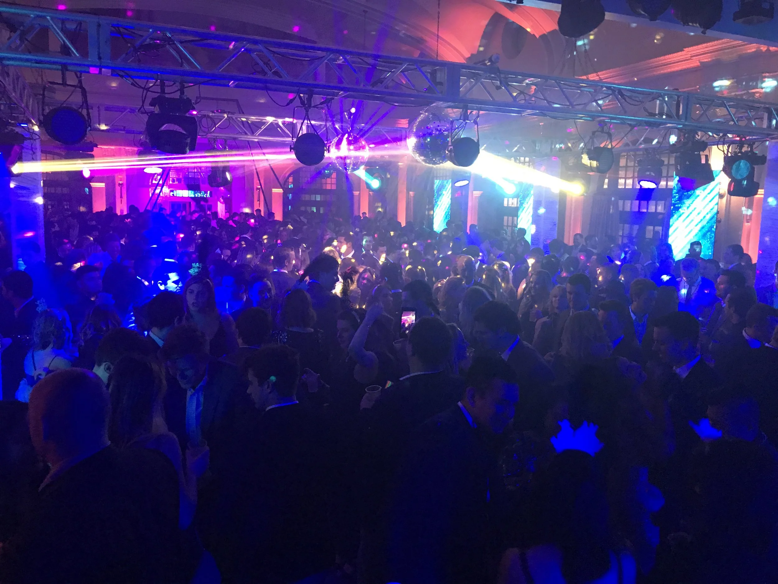 Crowded nightclub with people dancing under colorful lights and laser beams.
