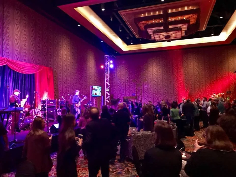 Live band performing at an indoor event with an audience watching, colorful stage lights, and a decorative ceiling.
