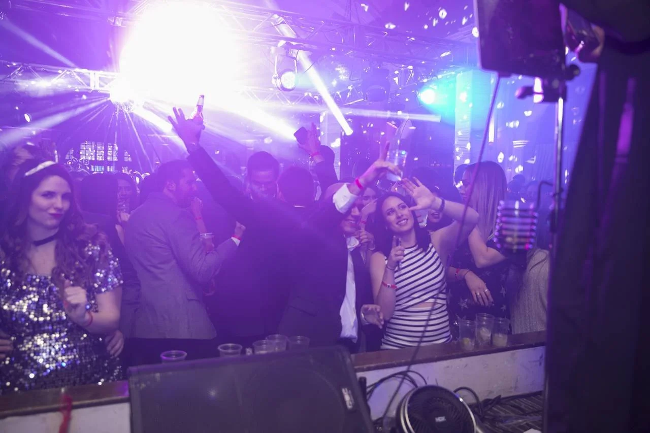 People dancing and celebrating at a nightclub with colorful lighting, wearing party attire.