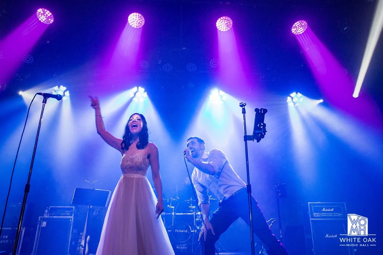 Female and male performers singing on stage with colorful spotlights at White Oak Music Hall.