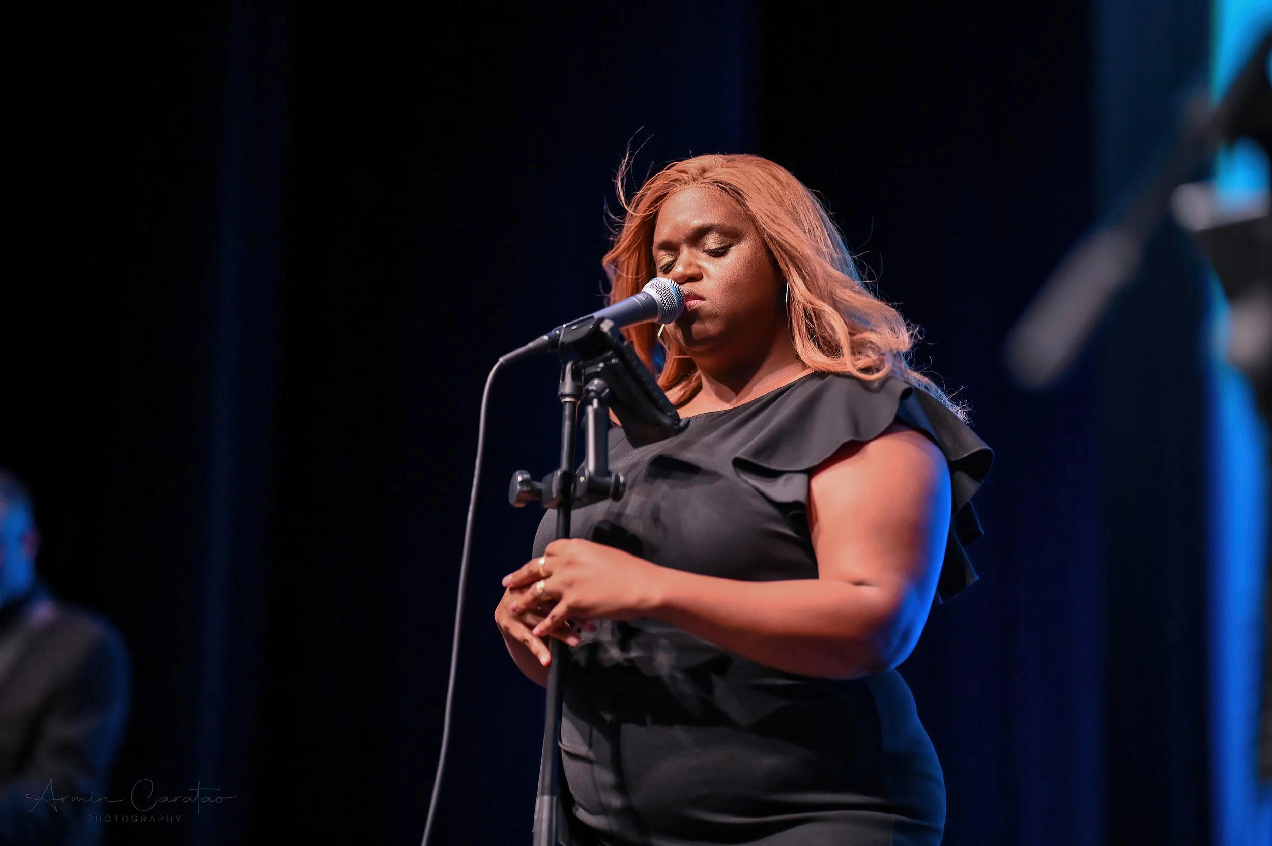 A woman in a black dress singing into a microphone on stage.