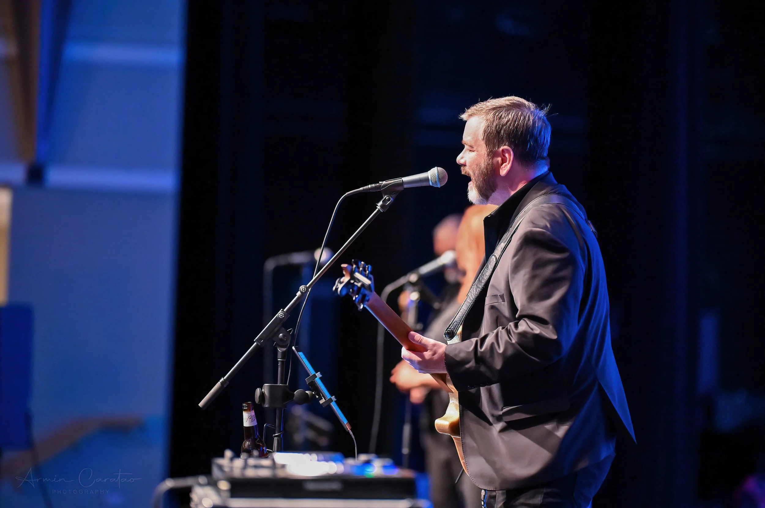 Musician performing on stage playing guitar and singing into a microphone