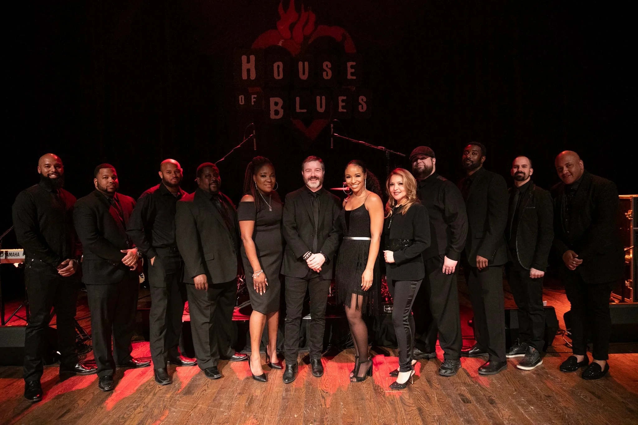 A group of people dressed in formal black attire posing together on a stage at the House of Blues.