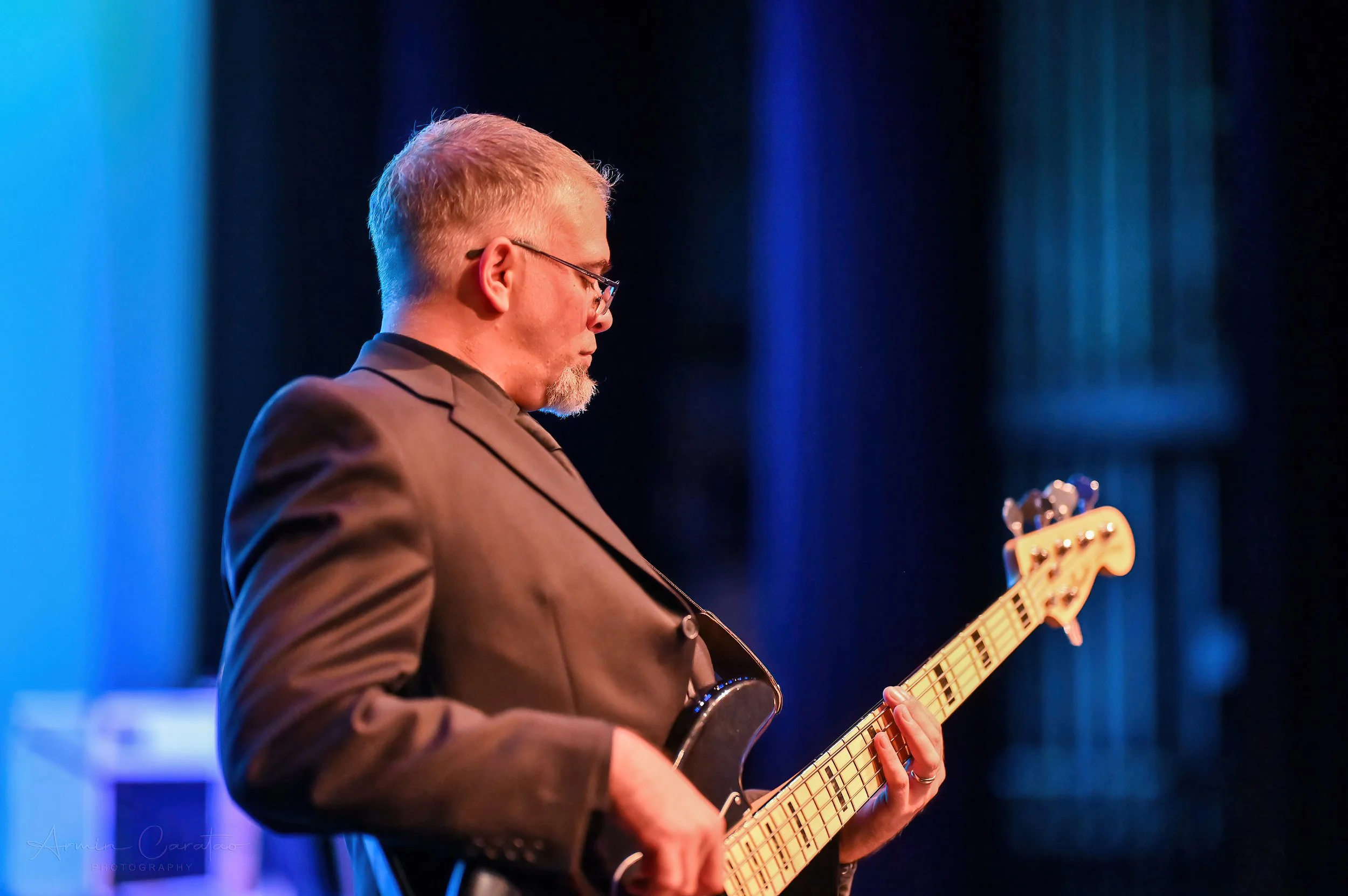 Man in a suit playing an electric bass guitar on stage.