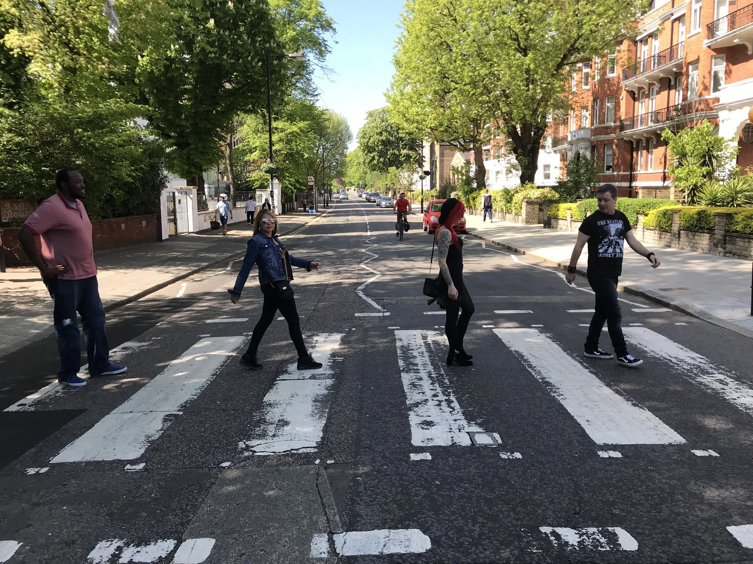 Four people crossing a street at a zebra crossing, surrounded by trees and buildings on a sunny day.
