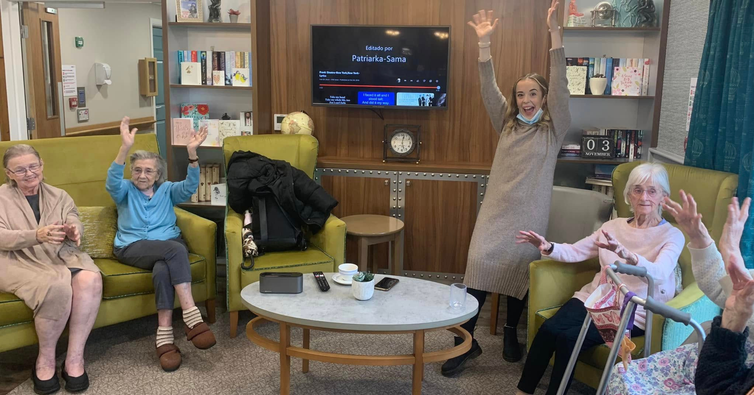 Elderly care home residents enjoying a group singing session with Stand Out Performing Arts Care Home Choir in Bristol, hands raised in celebration