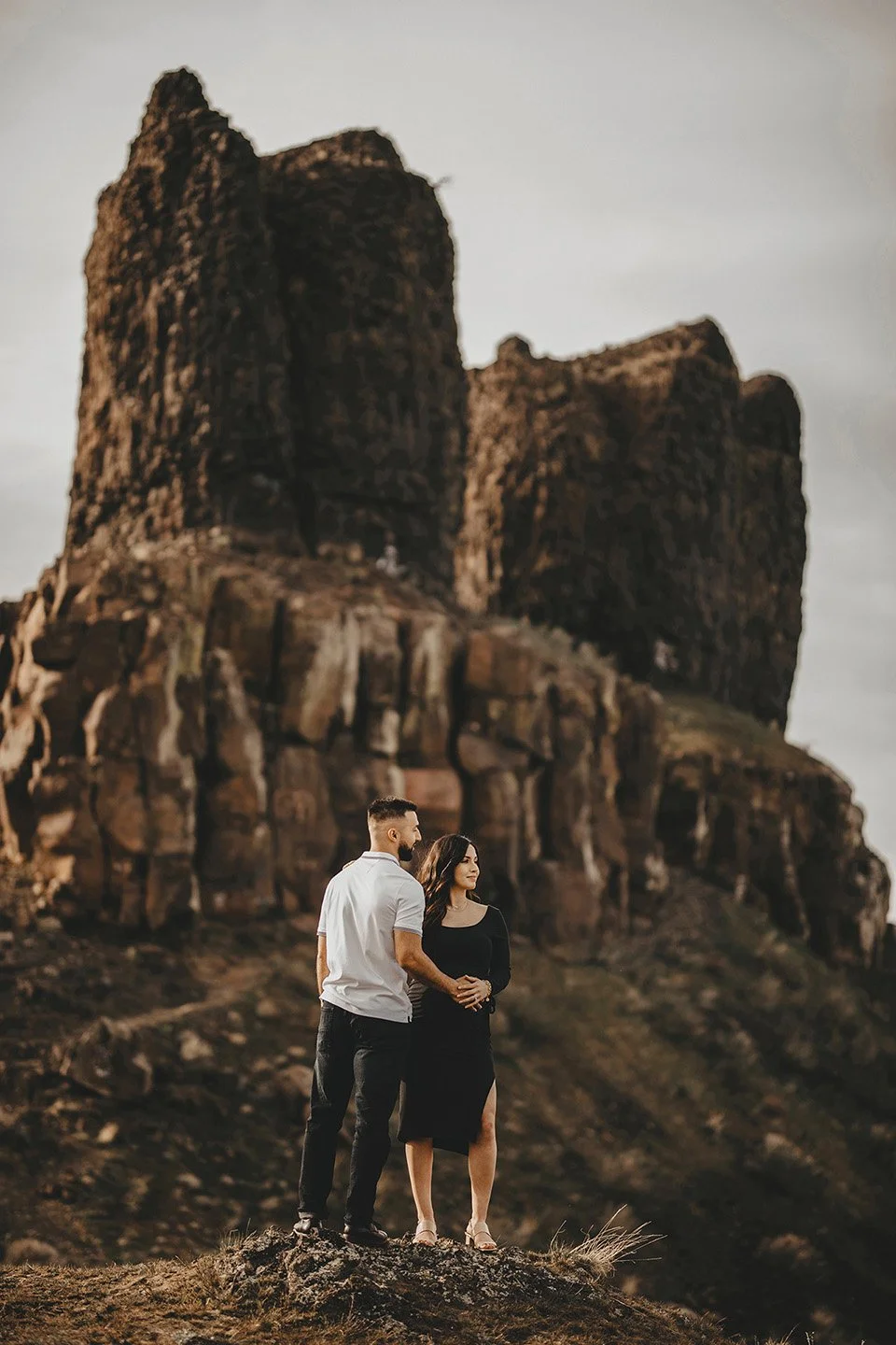 A peaceful and tender maternity portrait at Twin Sisters Rocks, where the couple stands close with their hands intertwined over her belly, looking out toward the horizon.