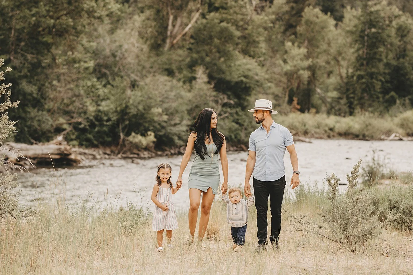 Natural family portraits in Naches, WA, walking together by the river holding their toddler’s hands.