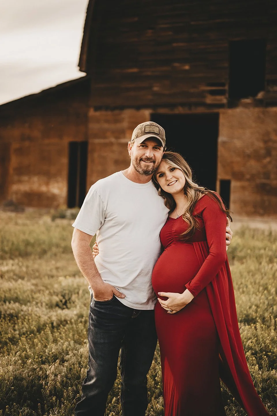 A warm and joyful maternity portrait in Sunnyside, where the expecting couple embraces and smiles at the camera with a classic barn setting behind them.