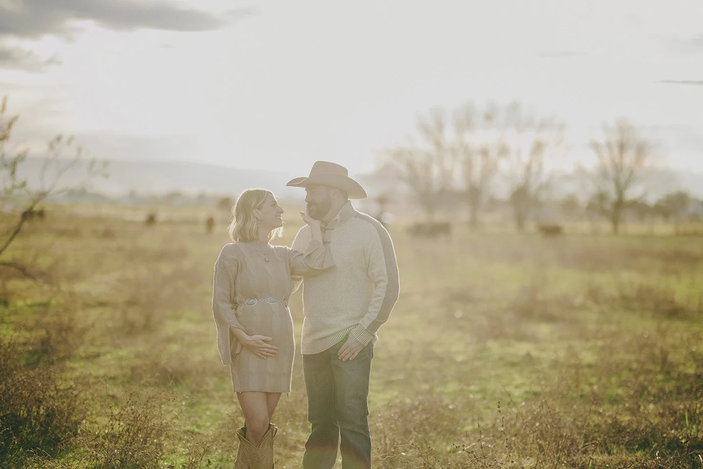 A warm winter maternity portrait in Sunnyside, where the mother-to-be gently holds her husband’s face while the soft sun glows behind them in their country pasture.