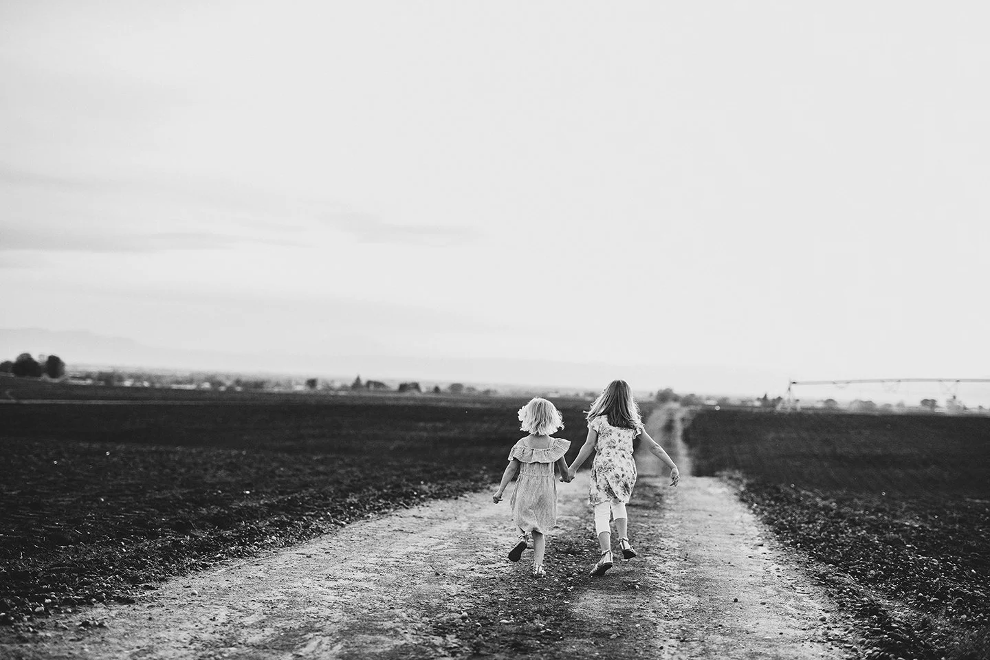 Sweet candid moment of two young sisters running through their family field during a Zillah,WA  sunset, captured in classic black and white.
