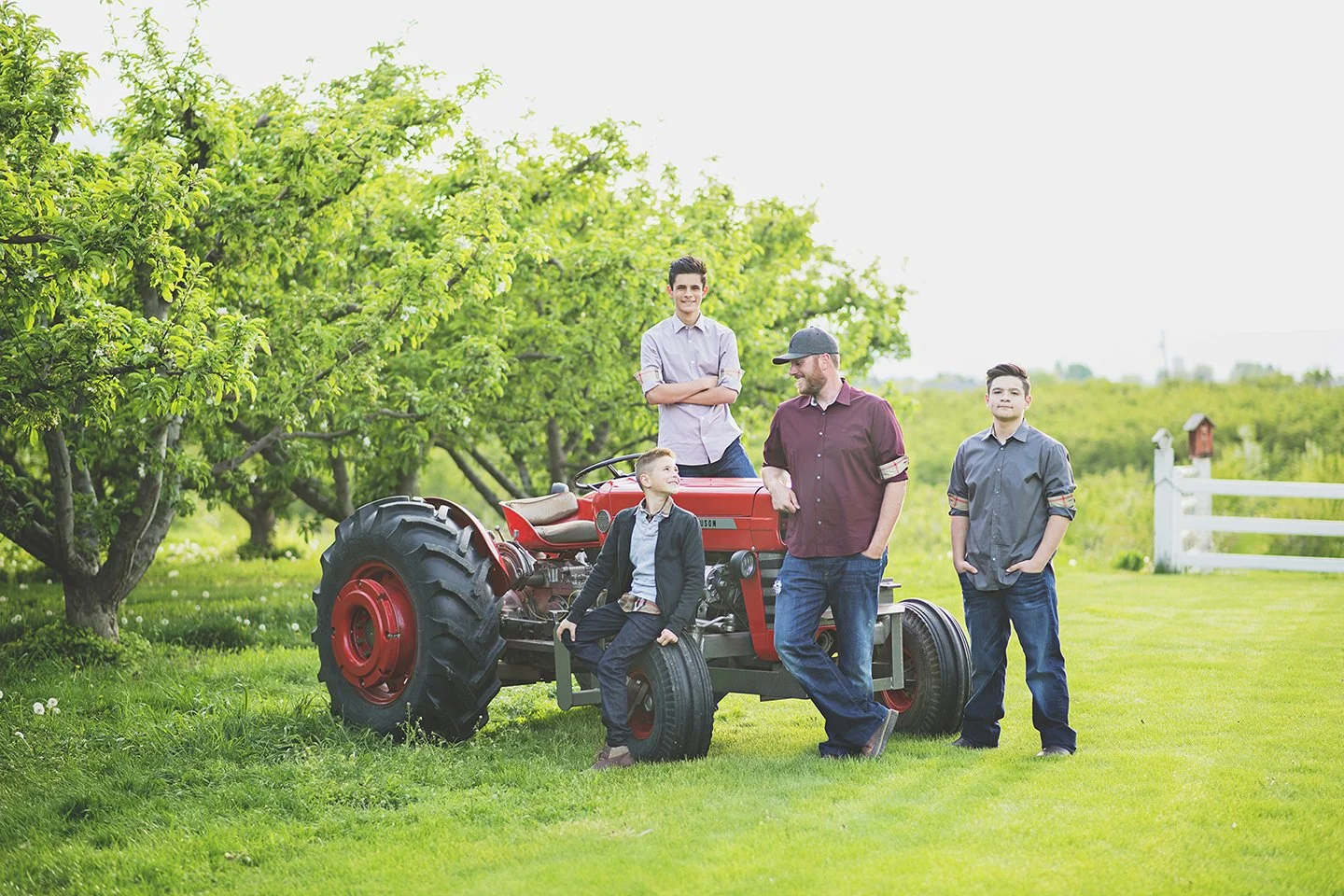 A warm father-and-sons moment in Zillah’s cherry orchards, standing by their tractor and white fence.