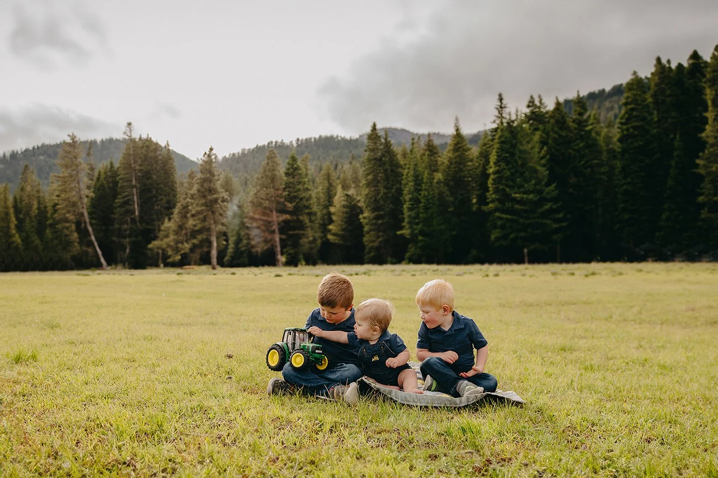 Playful sibling portraits in Naches, WA with tall trees and a little tractor toy.                        