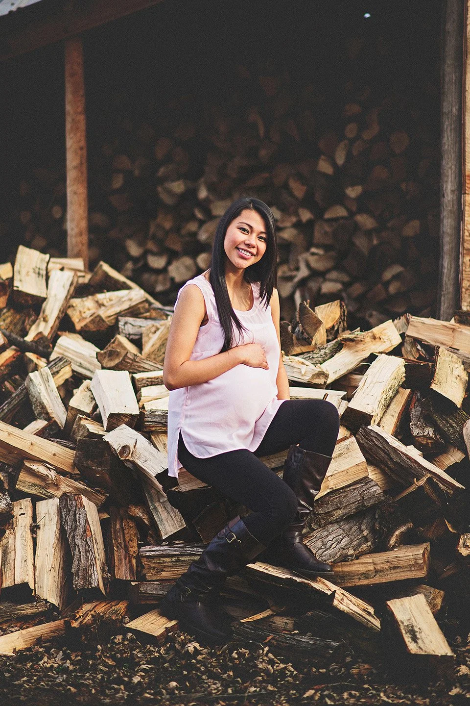 A soft and heartfelt maternity moment in Sunnyside, where the mother-to-be sits on rustic logs in a pink top, gently holding her belly with warmth and anticipation.
