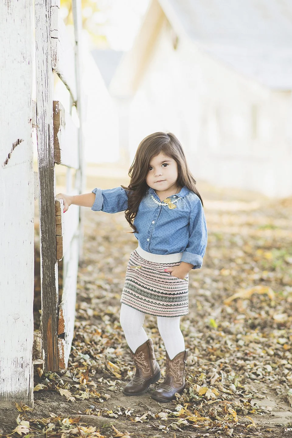 Country-style shoot of a sweet three-year-old at a white gate in Grandview,WA wearing denim and florals.
