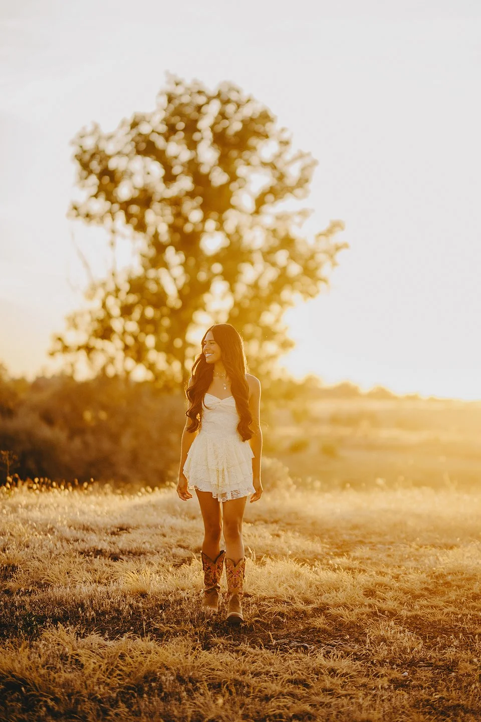 Outdoor senior portrait session in the Tri-Cities, sunset and gold tones shinning, senior girl wearing a short white dress and cowboy boots perfect for a summer evening shoot in Eastern, WA