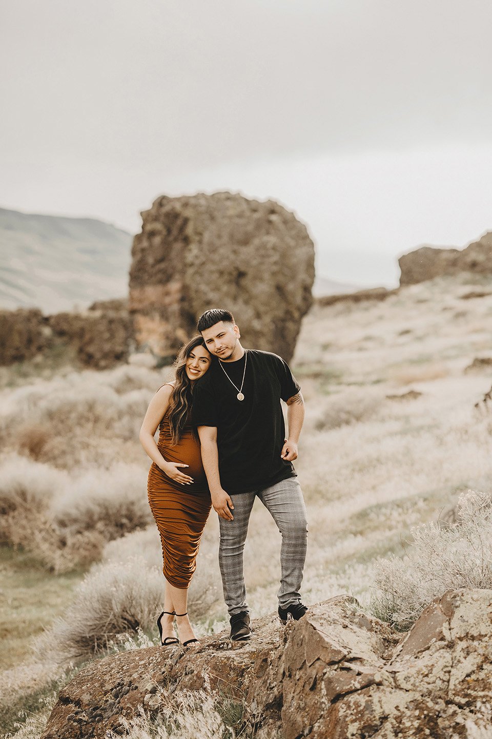 A joyful, sunlit maternity moment in Benton City, where the couple stands together on a rock, smiling big and leaning into each other with love and excitement.
