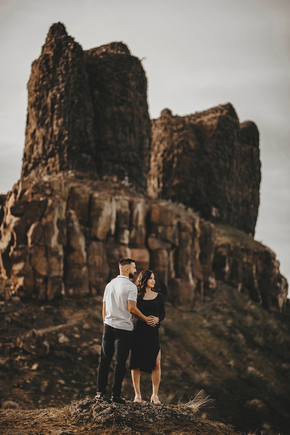 A peaceful and tender maternity portrait at Twin Sisters Rocks, where the couple stands close with their hands intertwined over her belly, looking out toward the horizon.