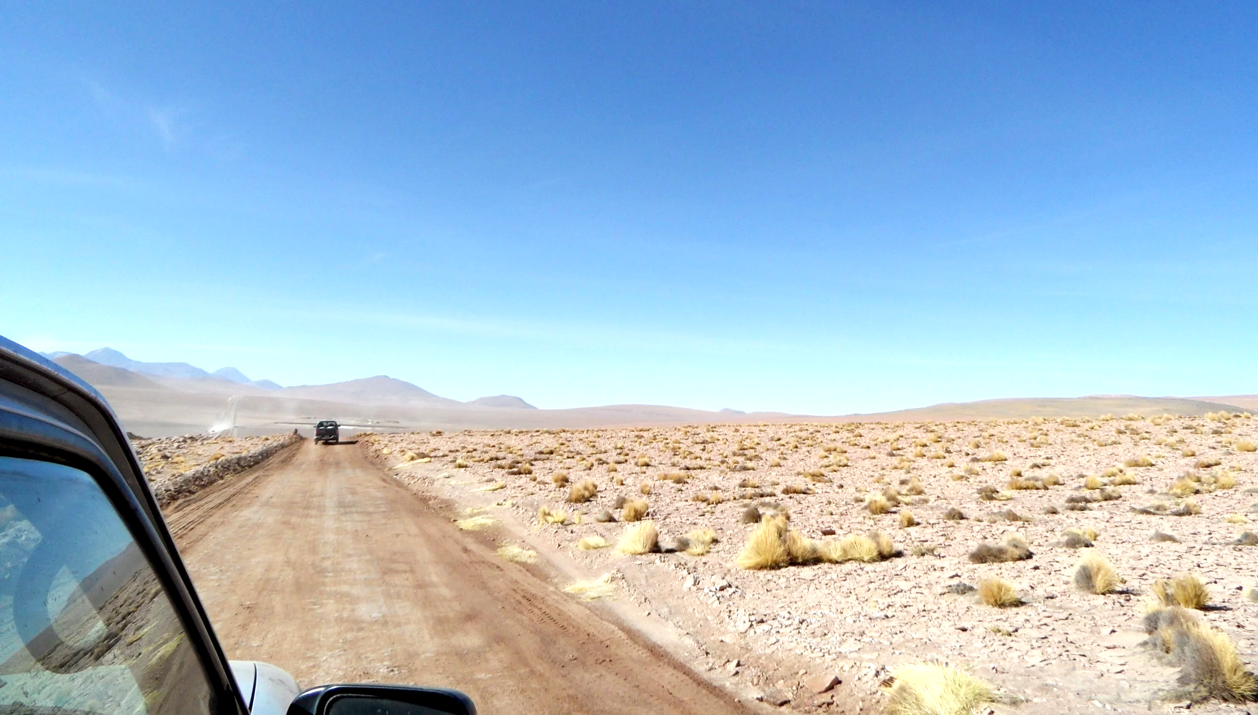 Carretera en un desierto con montañas en el horizonte y arbustos dispersos