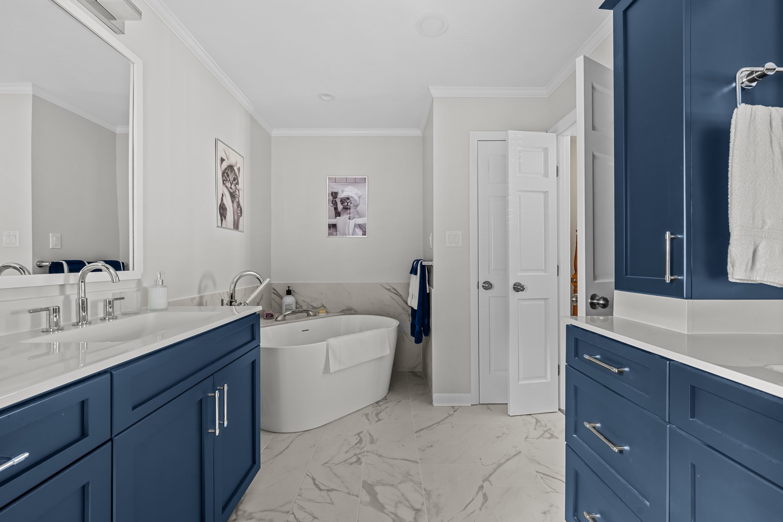 Primary bathroom featuring a blue vanity, tall storage cabinet, and freestanding soaking tub with a coordinated tile surround.