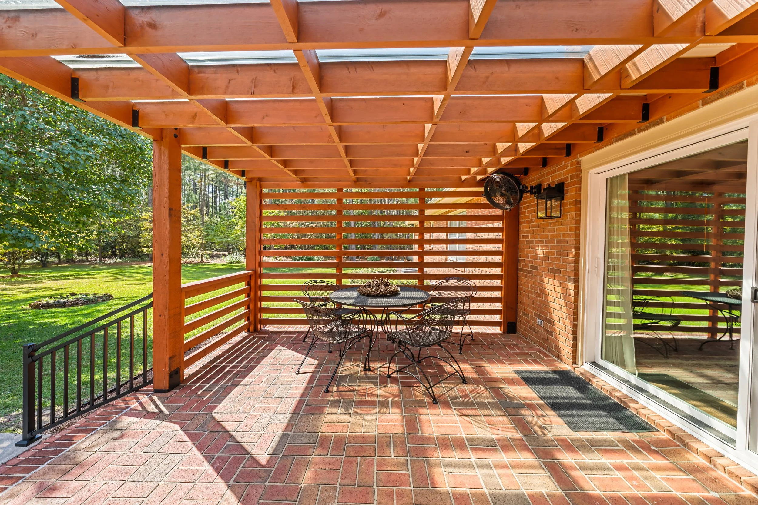 Outdoor dining space beneath the cedar pergola, featuring a translucent roof, horizontal privacy screening, and a brick patio.