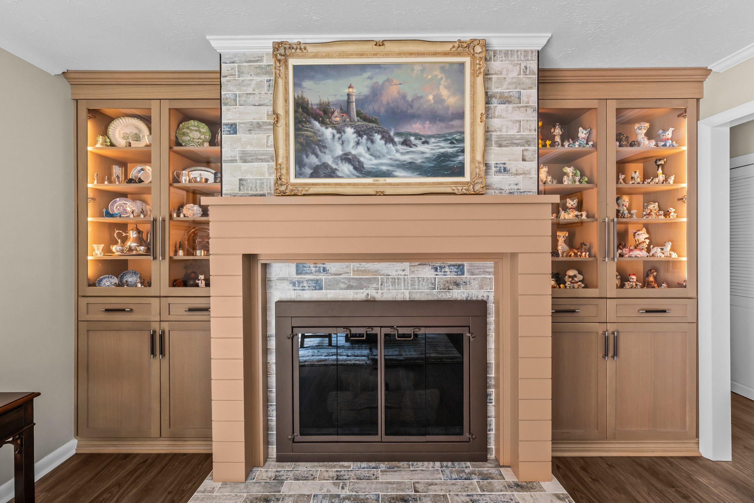 Remodeled fireplace with a tile surround, substantial mantel, and matching illuminated display cabinets with enclosed storage below.