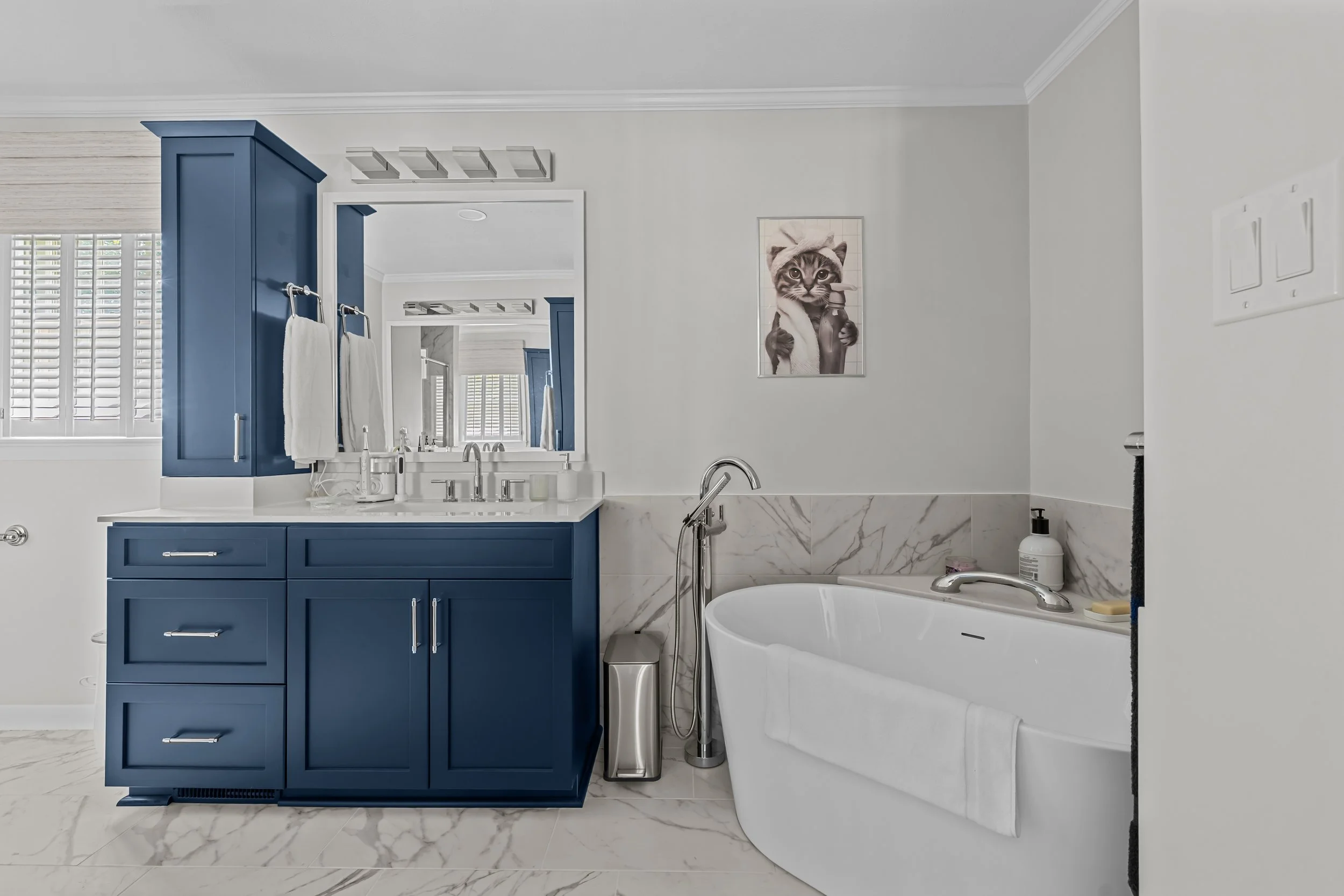 View through the primary bathroom showcasing blue cabinetry, expansive counter space, and a freestanding tub.