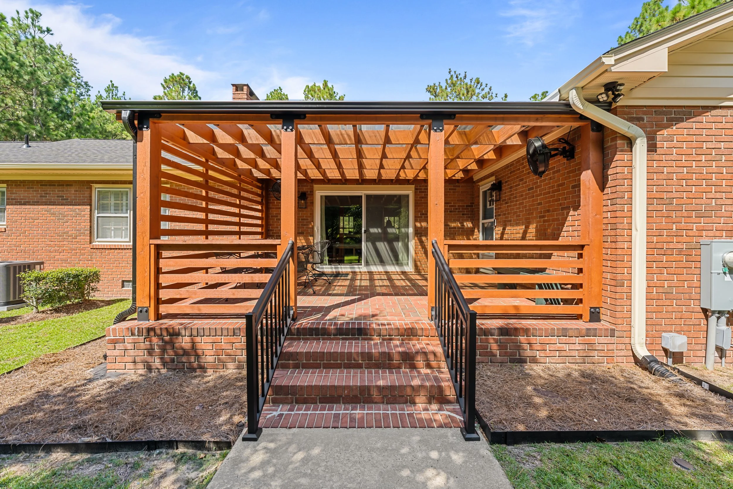 Cedar pergola framing the rear entrance, with horizontal privacy screening, brick steps, and black metal handrails.