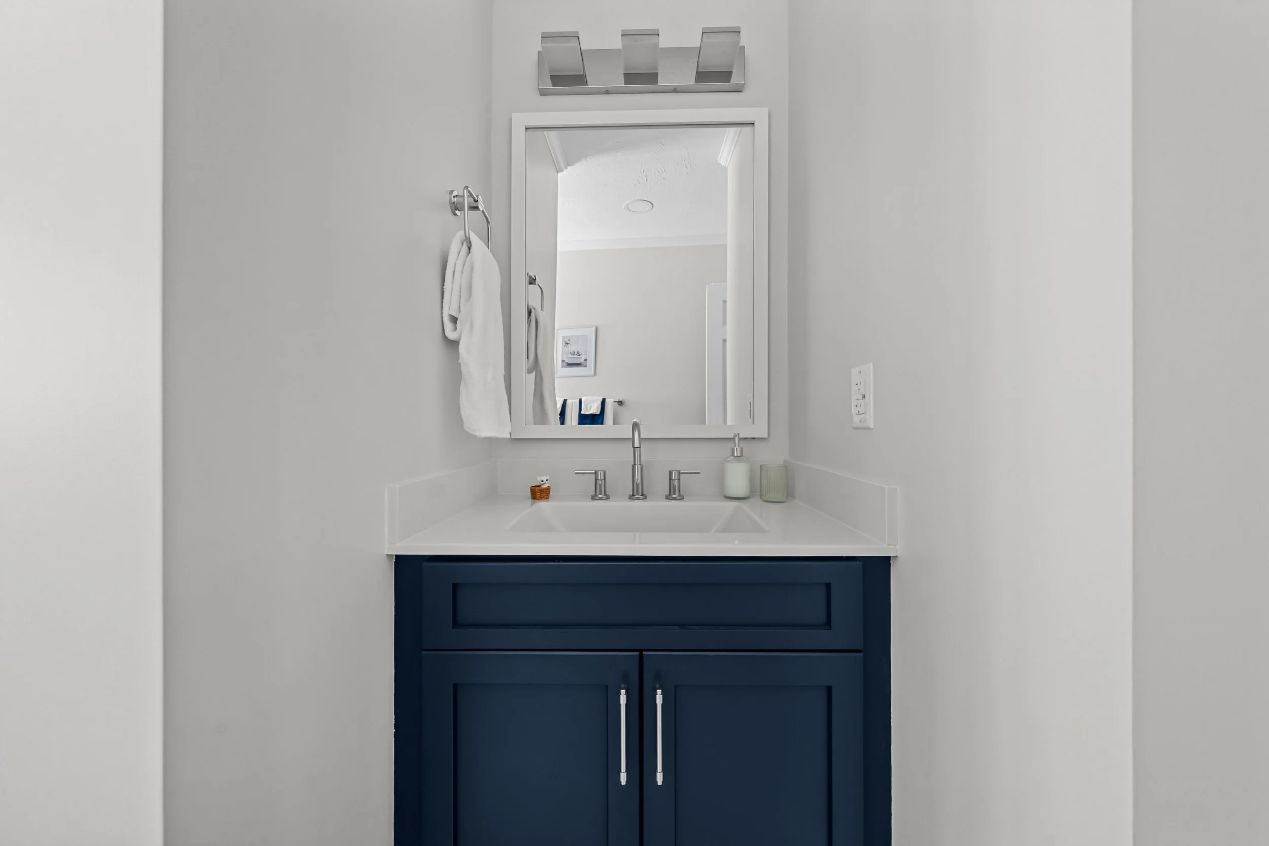 Blue bathroom vanity paired with a white countertop, chrome fixtures, and coordinating mirror and lighting.