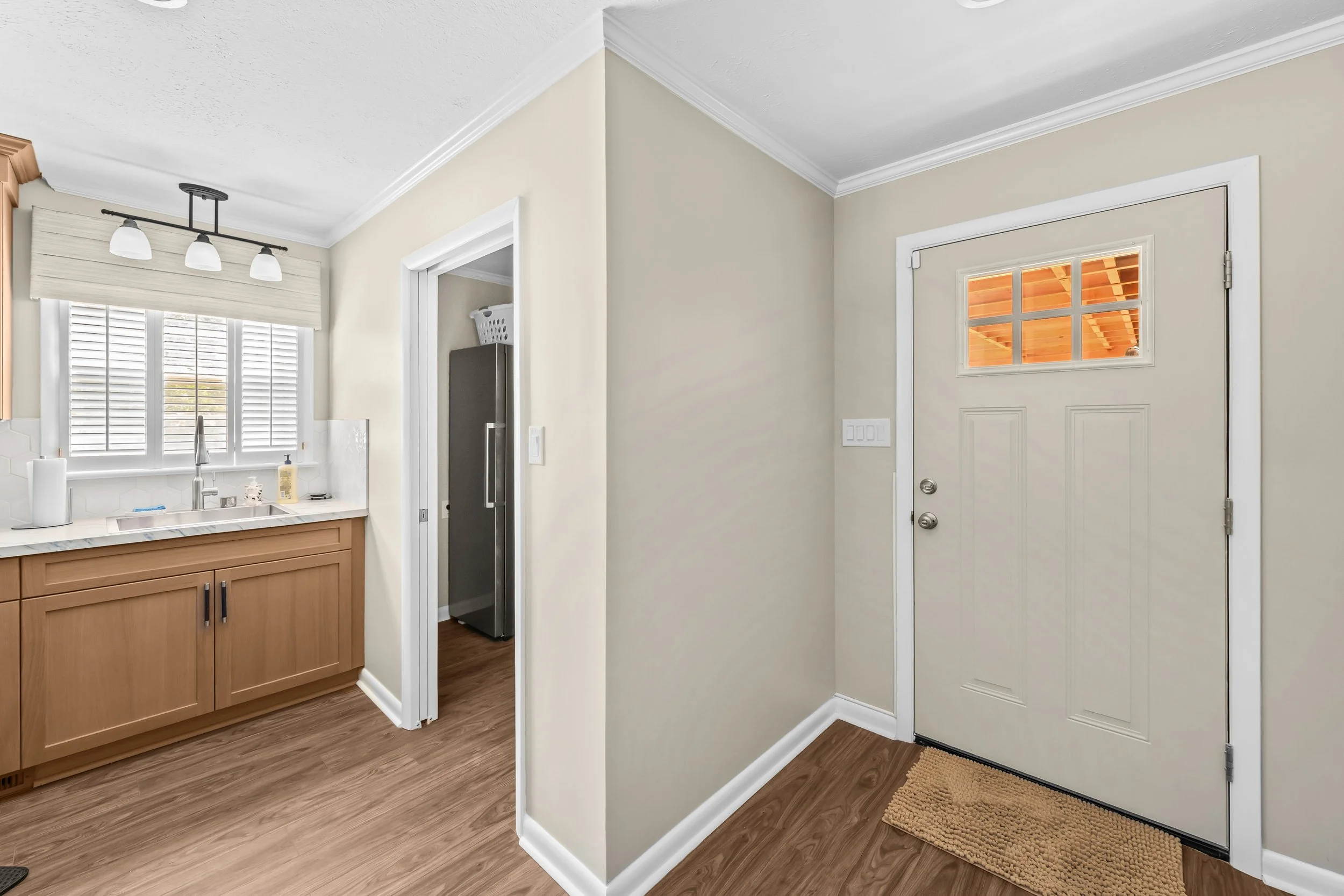 Updated rear entrance and utility room featuring a windowed exterior door, wood-look flooring, and built-in cabinetry with a sink.