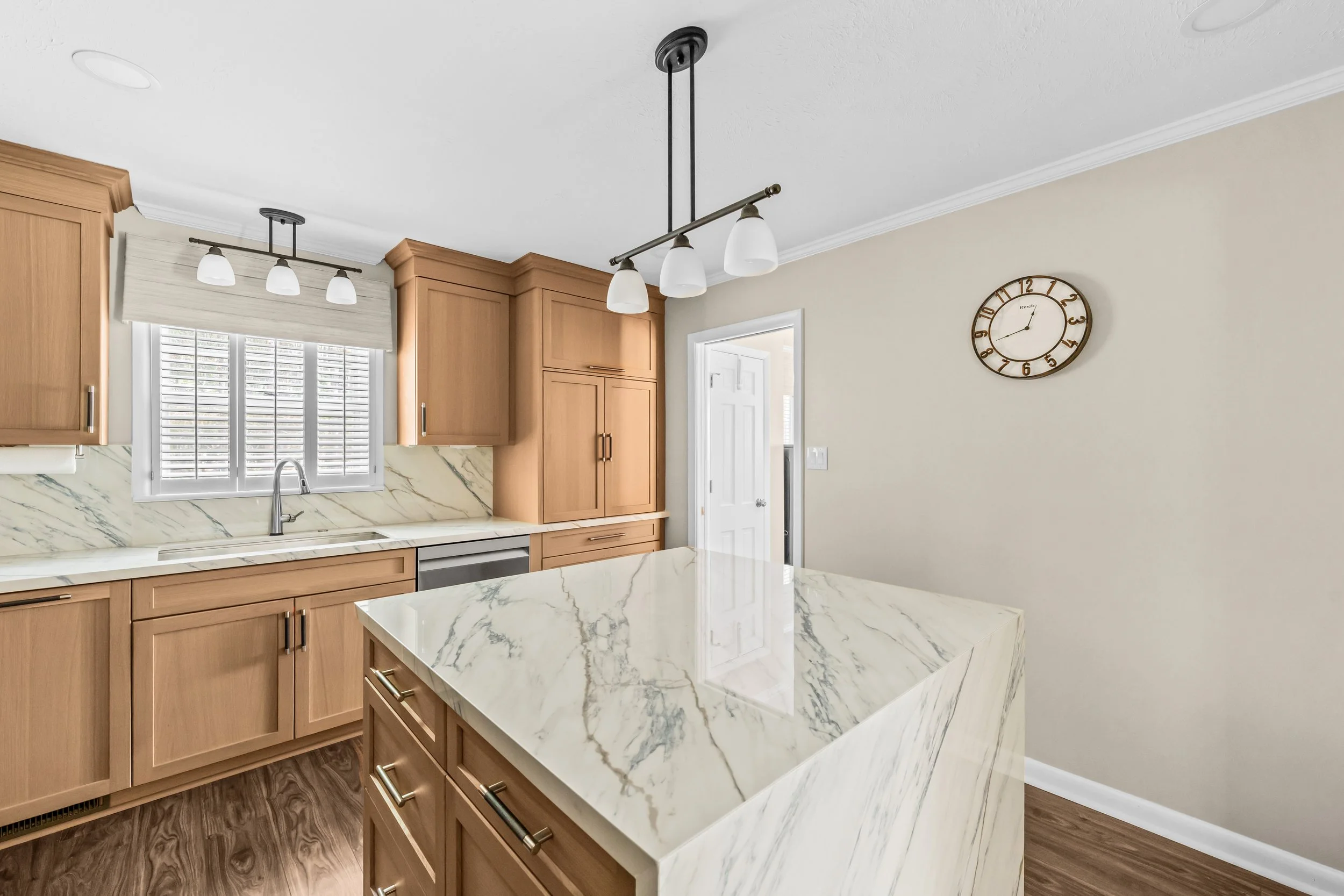 Remodeled kitchen featuring warm wood cabinetry, a waterfall island, veined countertops, and a coordinated full-height backsplash.