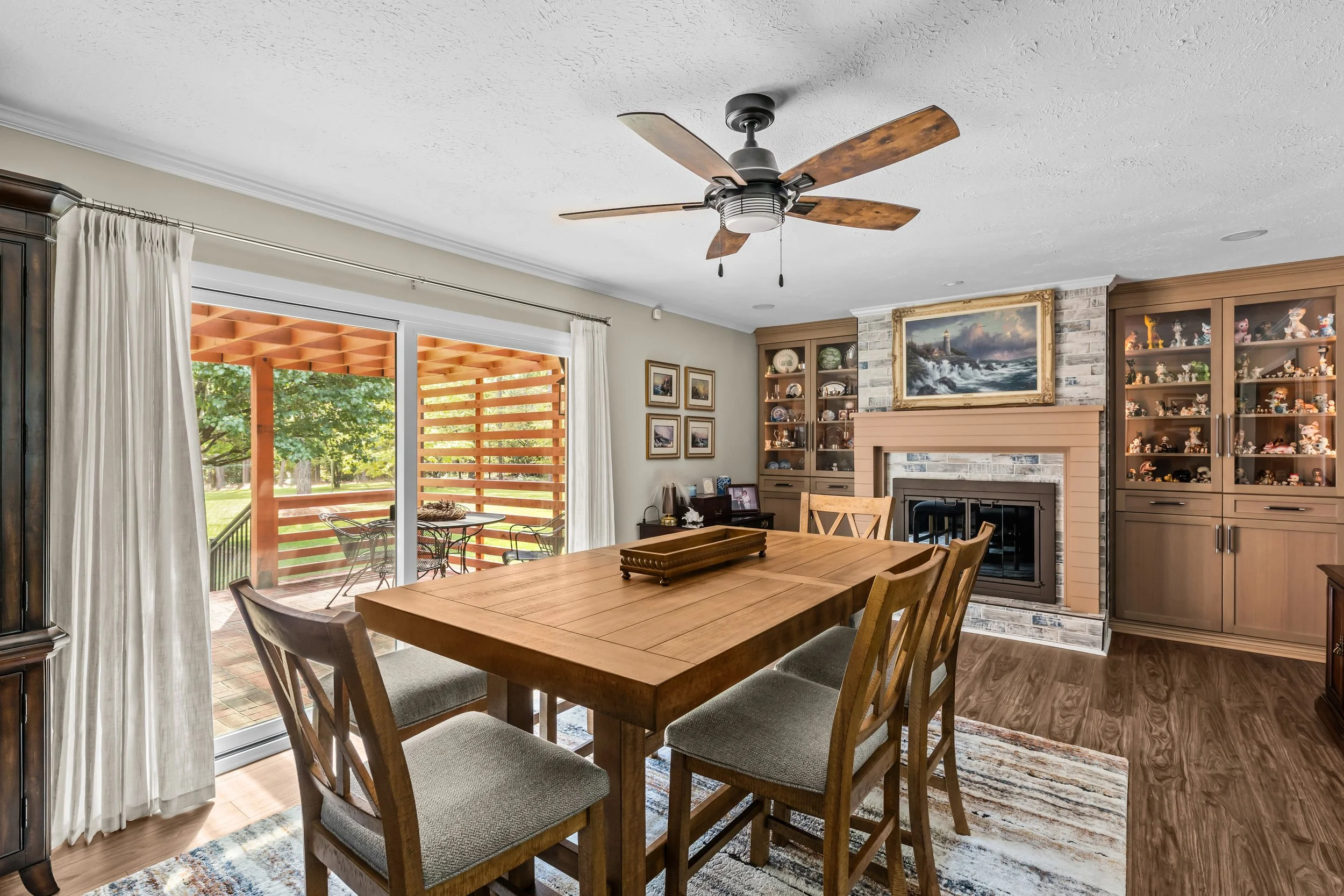 Dining space featuring an updated fireplace, illuminated display cabinets, and wide sliding glass doors overlooking the cedar pergola.