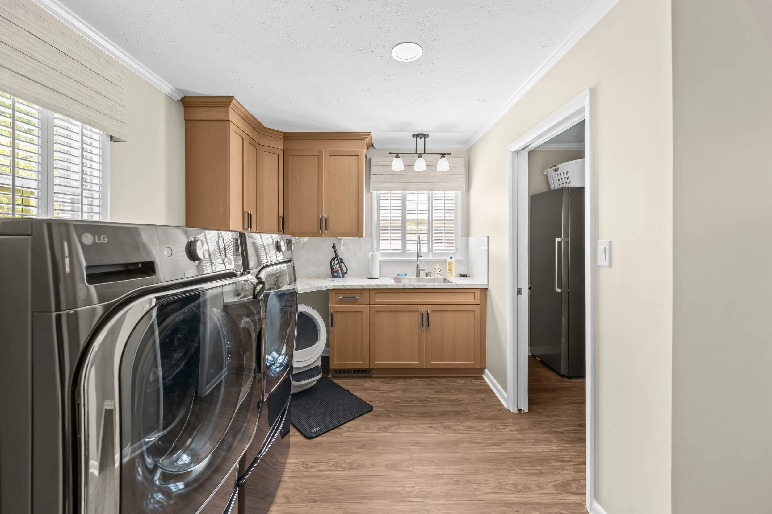 Renovated laundry room with front-loading appliances, wood-look flooring, and a utility sink with coordinating cabinetry.
