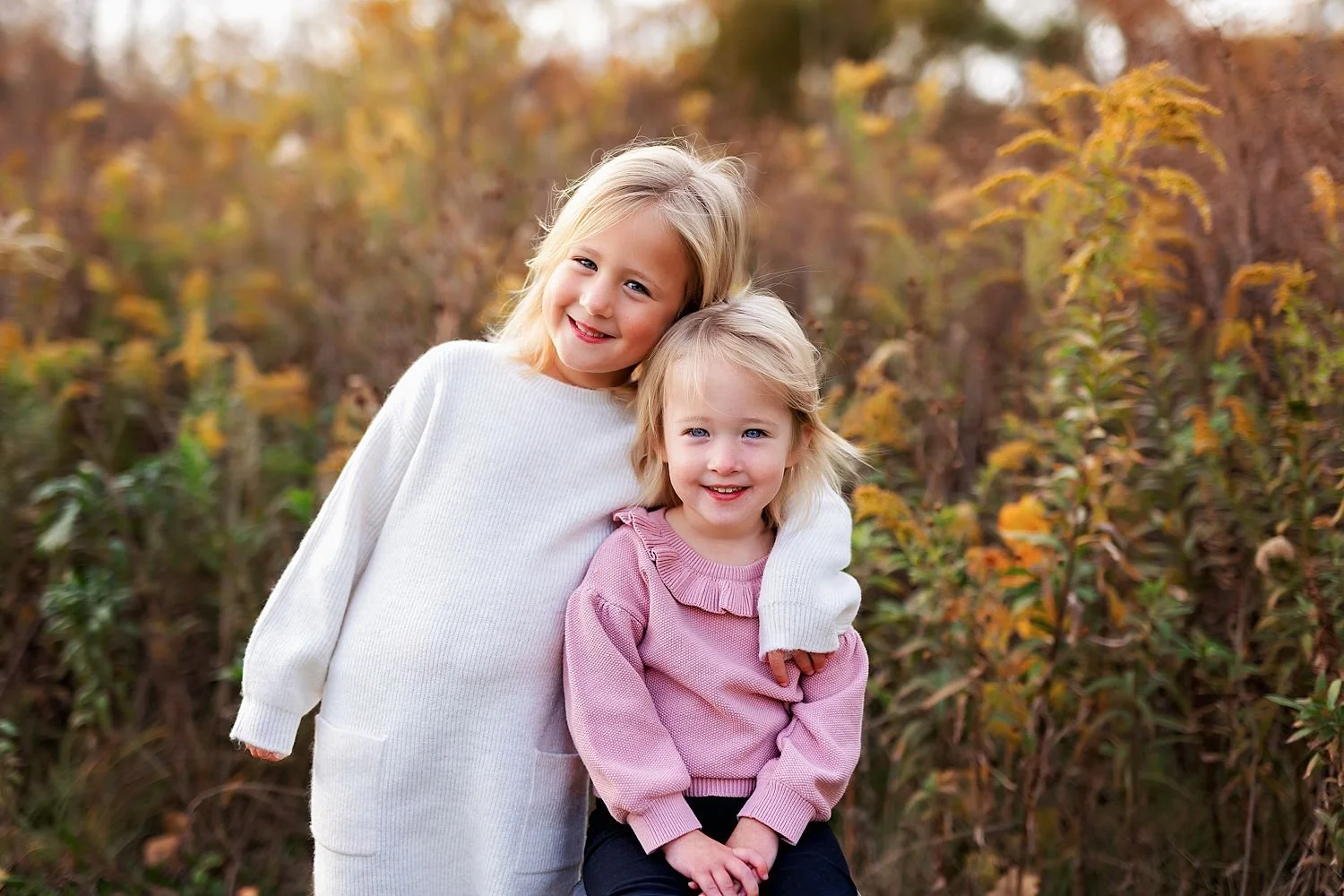 Young sisters smiling in a field during their Carmel family photography session