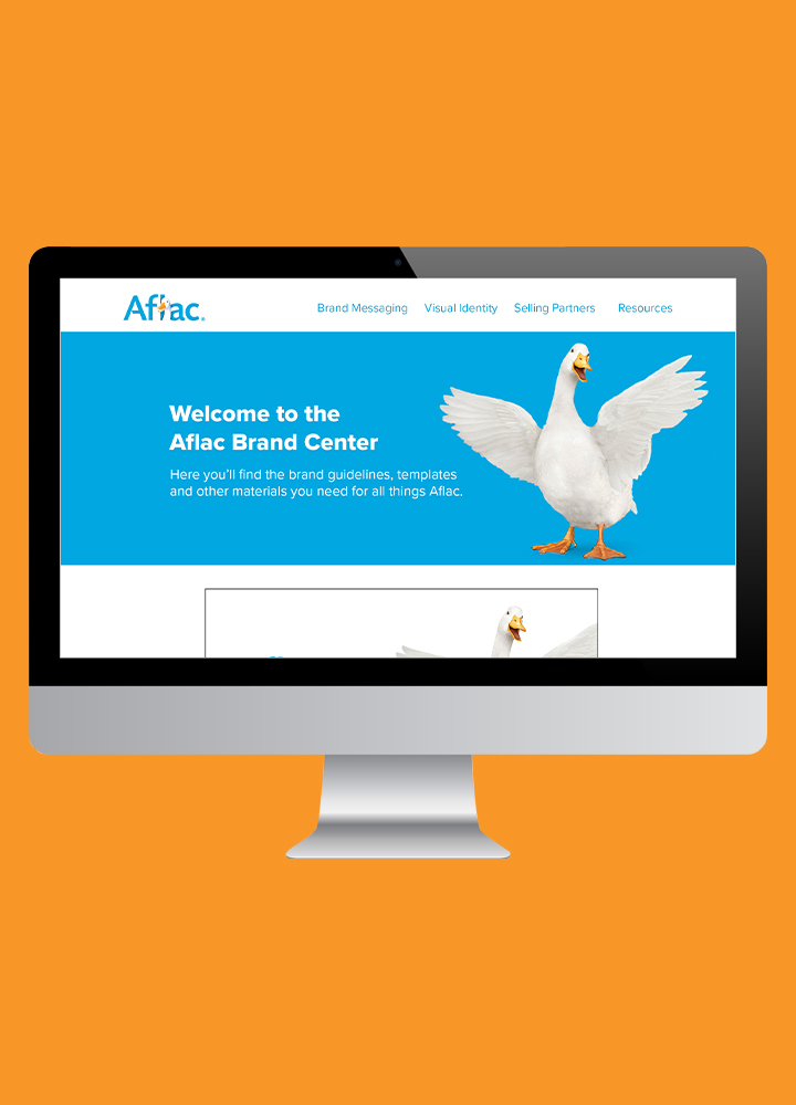 Computer monitor displaying the Aflac Brand Center website with a large image of a flying goose on a blue background, set against an orange backdrop.