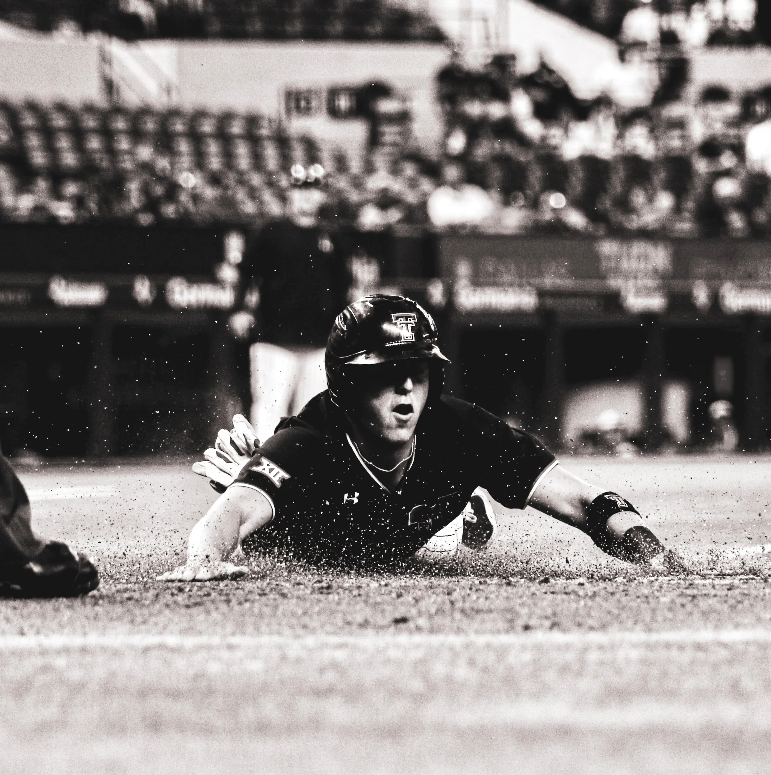 Black and white photo of a baseball player sliding into home plate, with a crowd of spectators in the background.