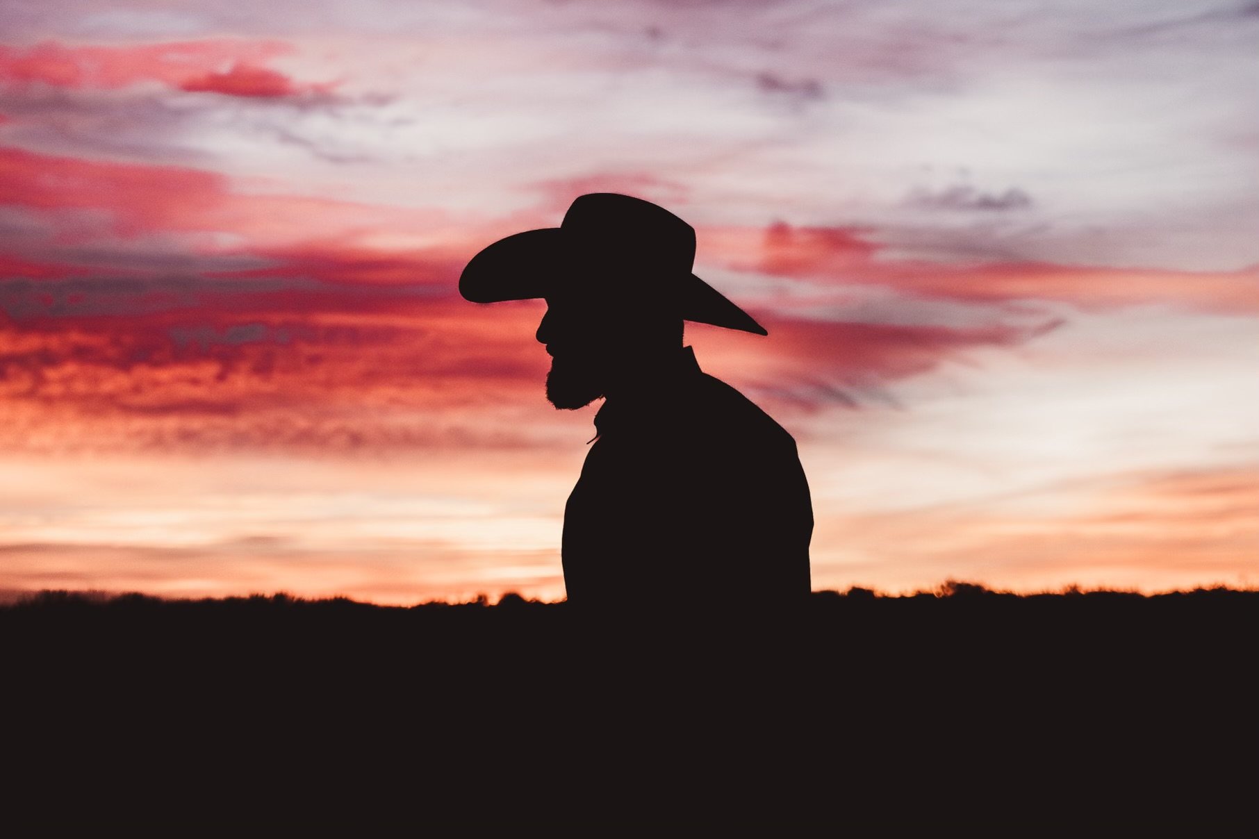 Silhouette of a man wearing a cowboy hat against a colorful sunset sky.