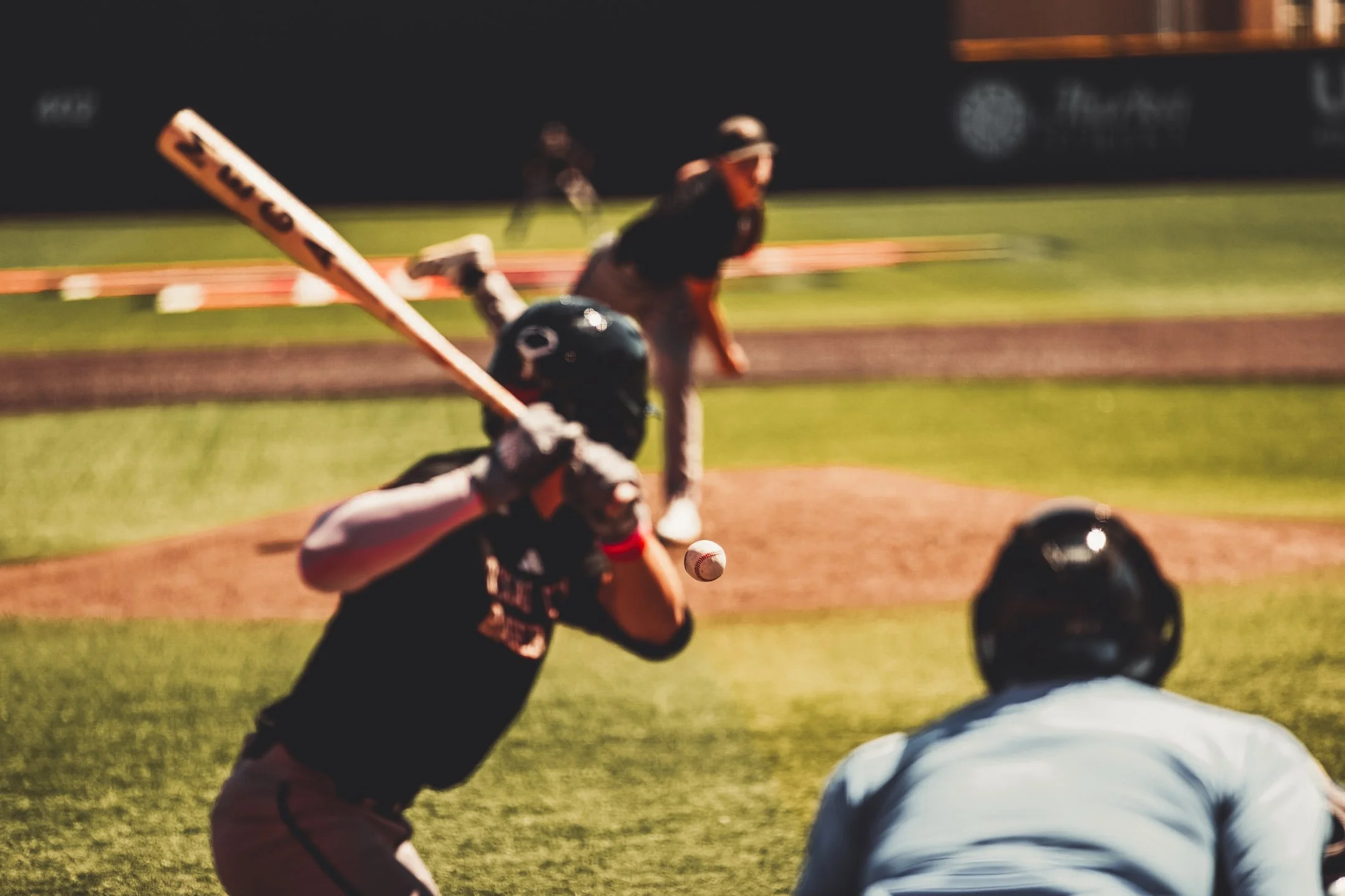 A baseball game in progress with a batter swinging at a pitch, an umpire behind the batter, and a player in the outfield.