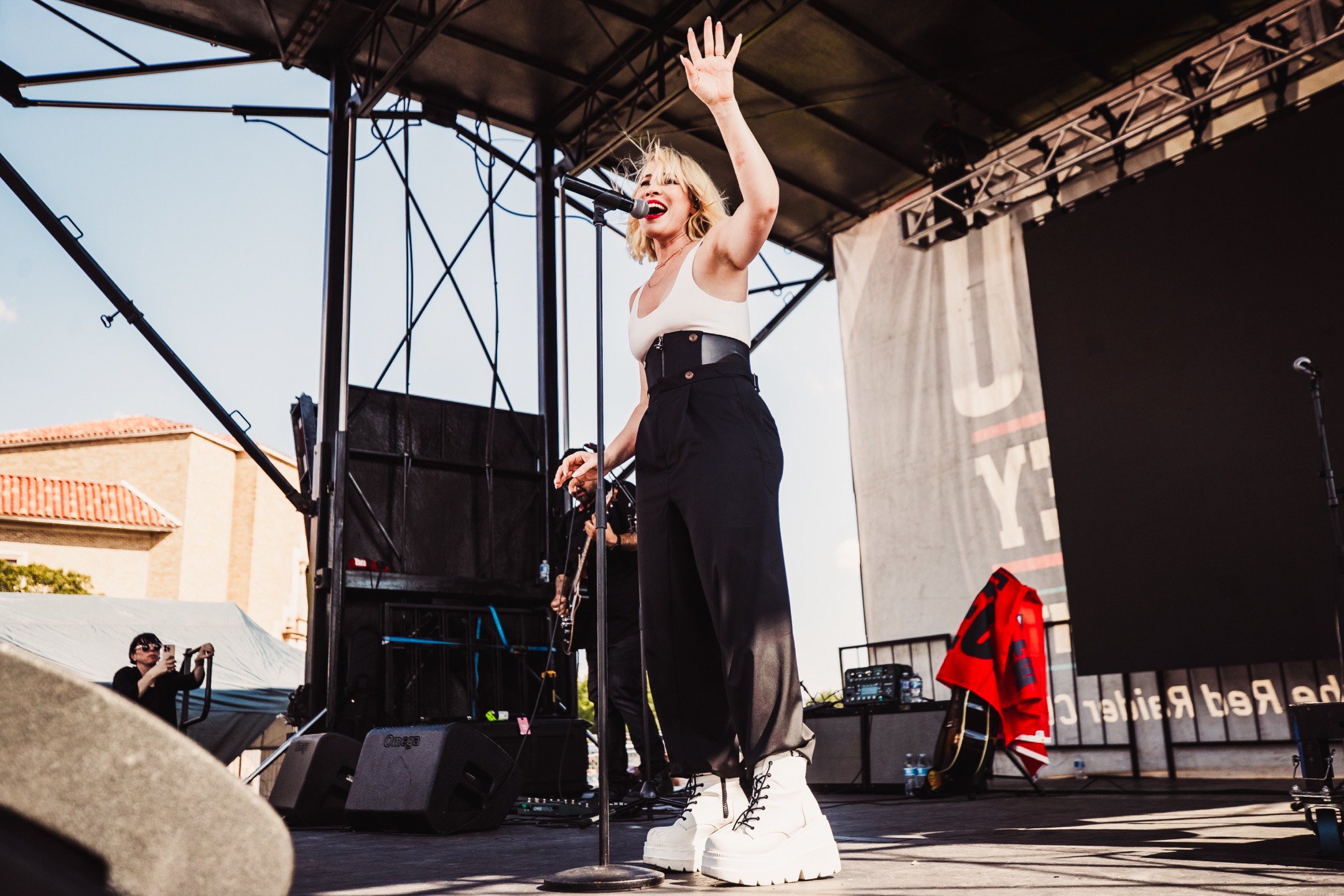 Female singer performing on an outdoor stage with a guitar player in the background