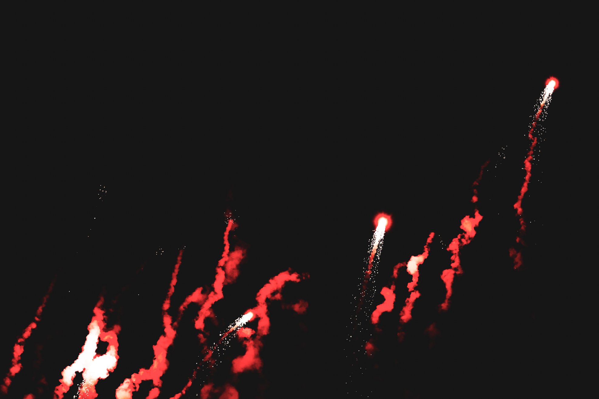 Fireworks exploding in the night sky with red and white streaks against a dark background.