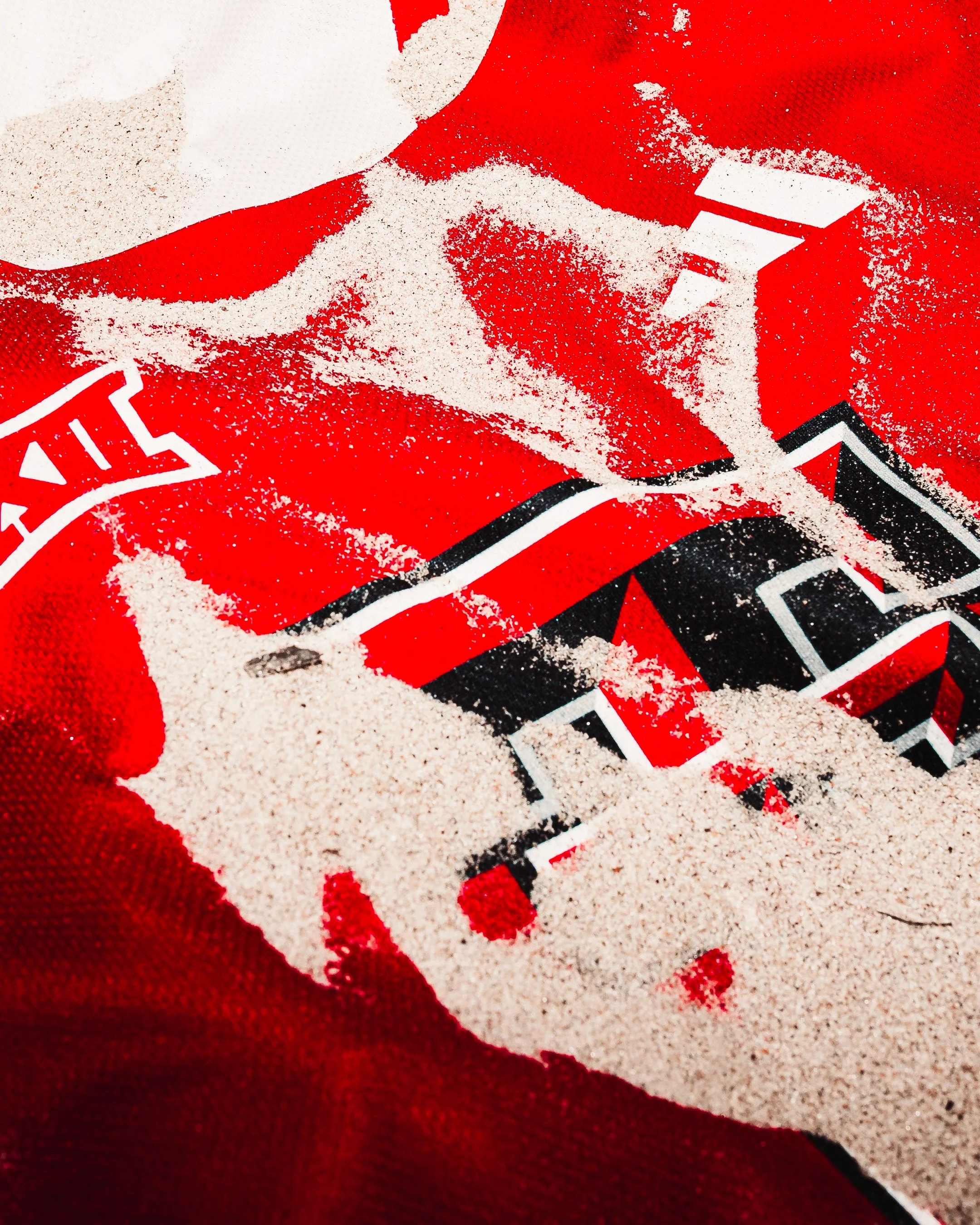 Close-up of a red sports jersey with black and white details, partially covered with light-colored sand.