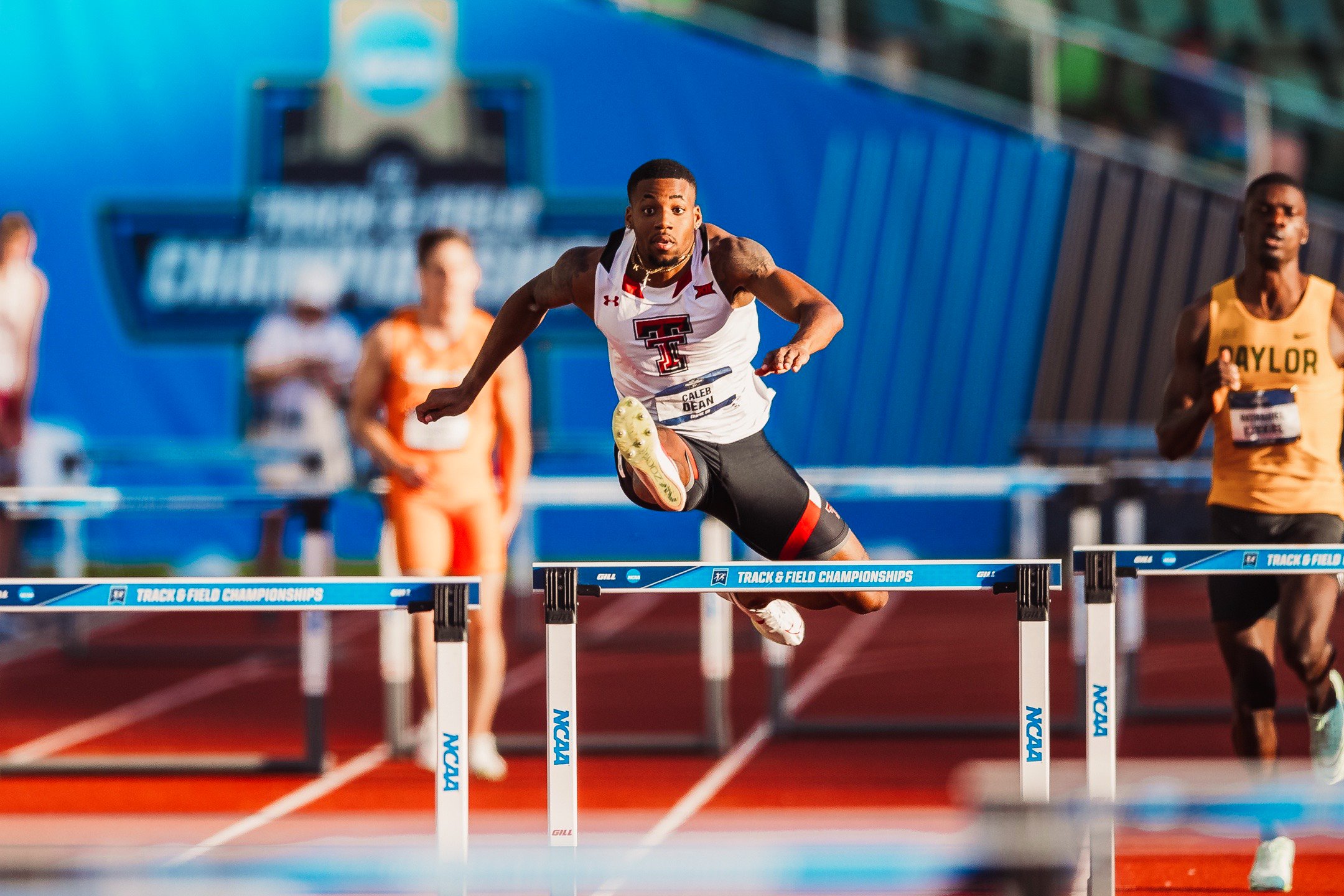 A male athlete in a Texas Tech uniform clears a hurdle during a track and field event at the NCAA championships.