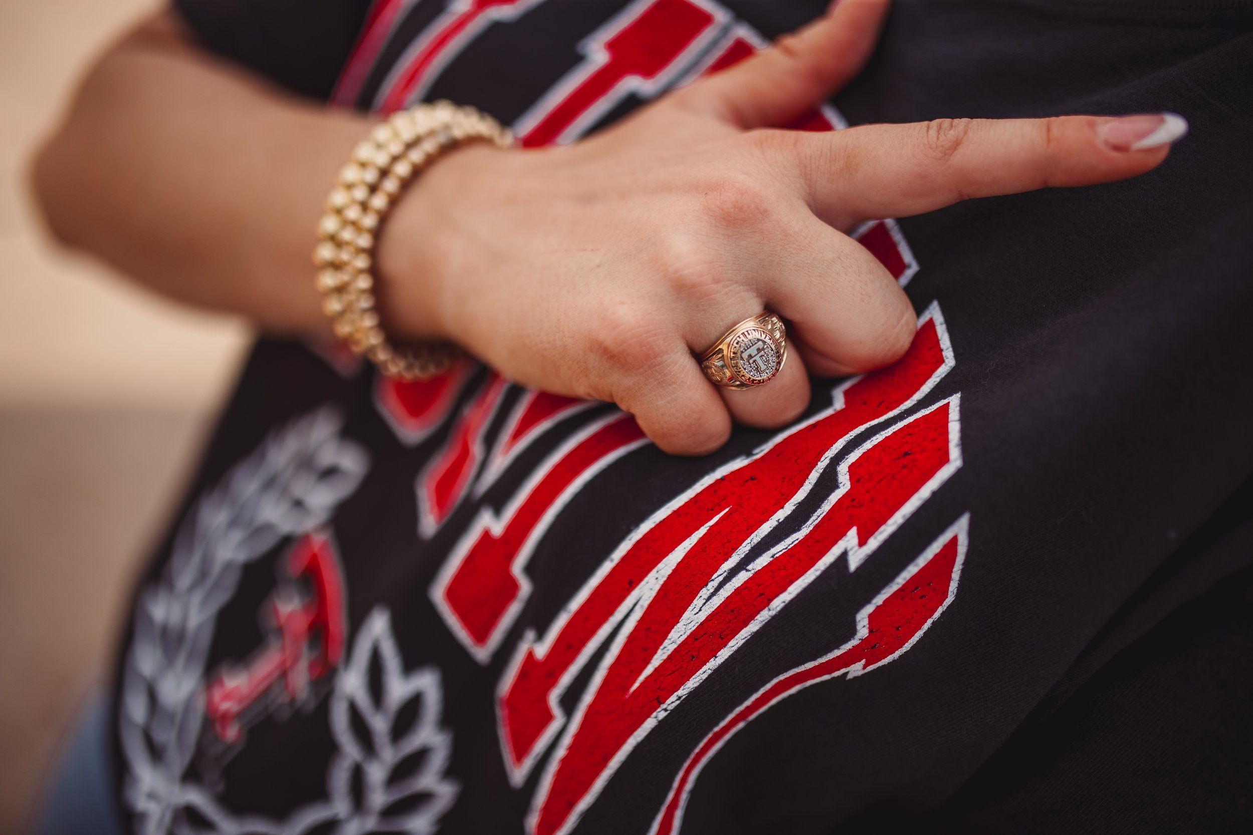 Close-up of a person's hand resting on a black and red fabric, wearing a Catholic ring and a pearl bracelet.