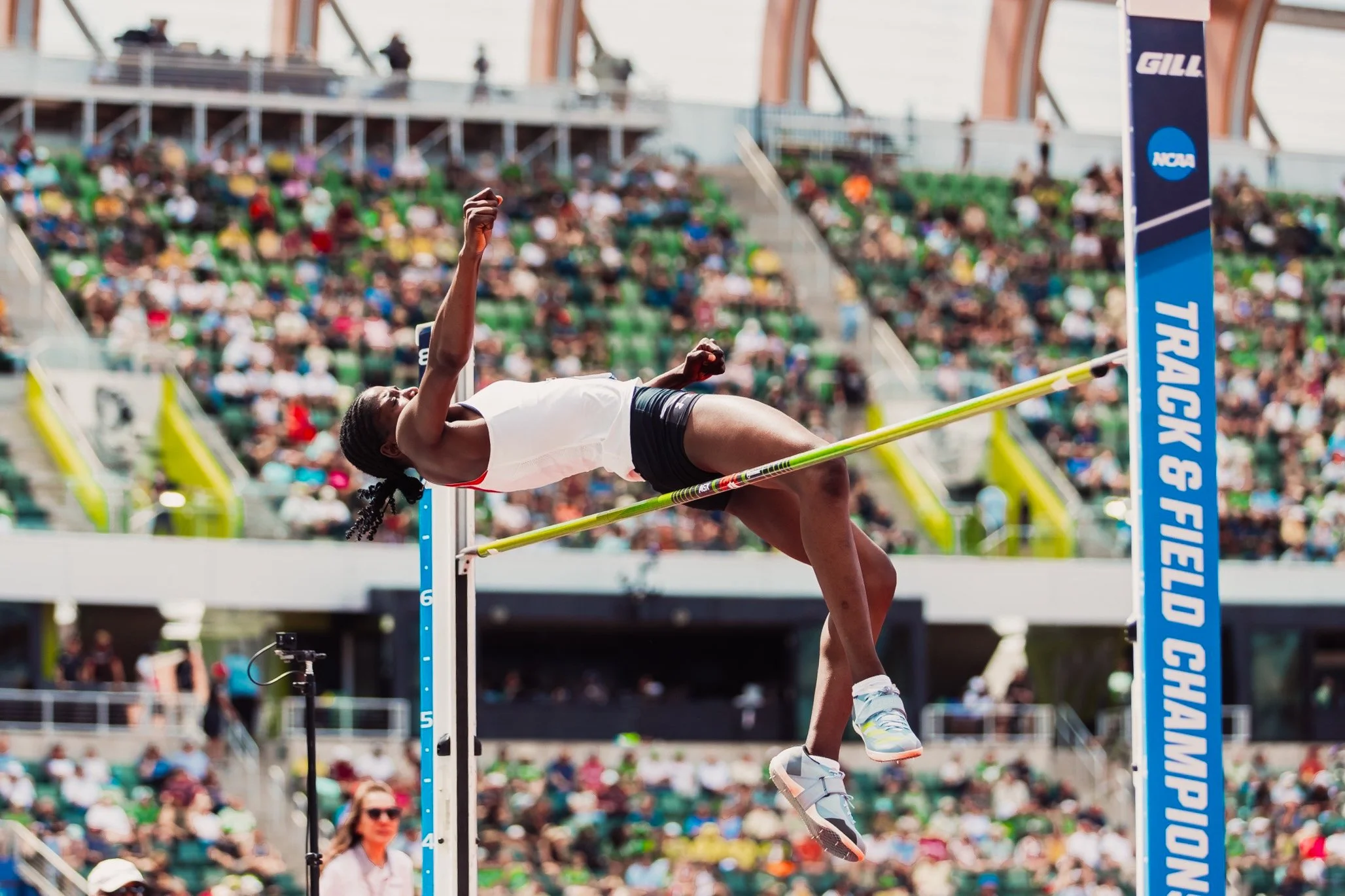 Female high jumper clearing the bar during a track and field event at the NCAA Championships conference in a stadium filled with spectators.