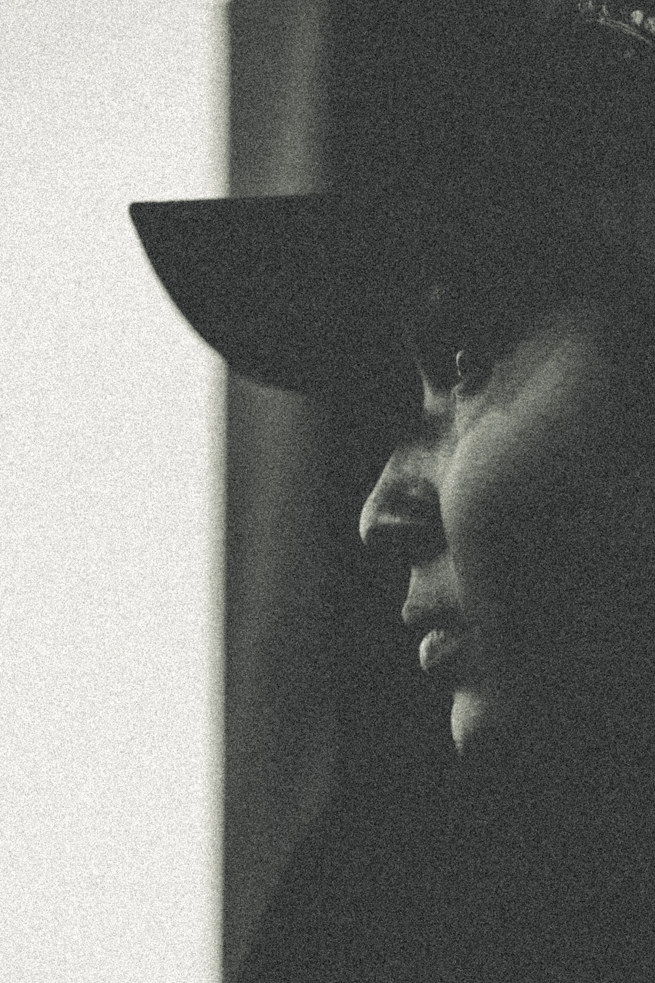 Black and white close-up of a person's profile wearing a hat, with a serious expression.