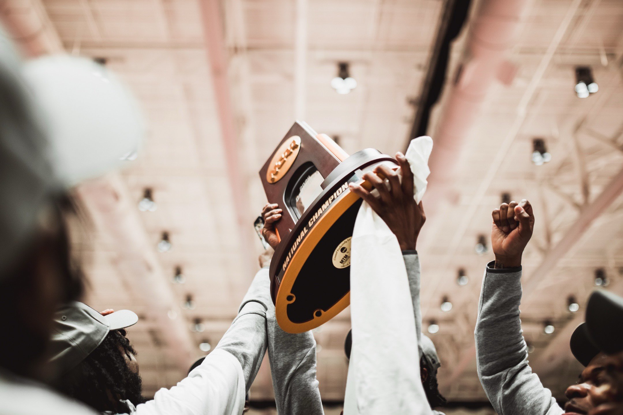 A sports team holding up a championship trophy inside a gymnasium with a high ceiling.