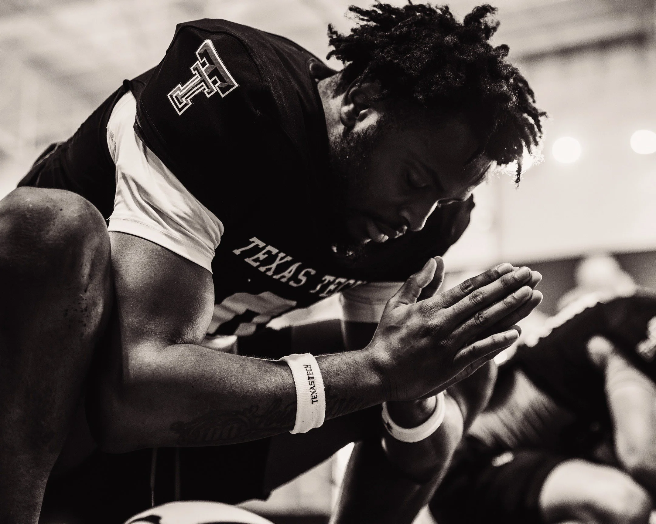 A football player in a Texas Tech jersey kneeling with hands together in prayer.